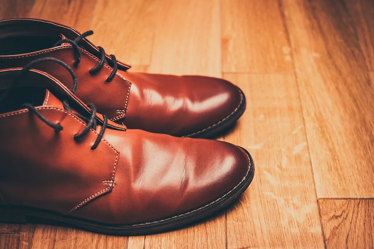 A pair of brown leather lace-up boots on a wooden floor, cut off by the left edge of the photo