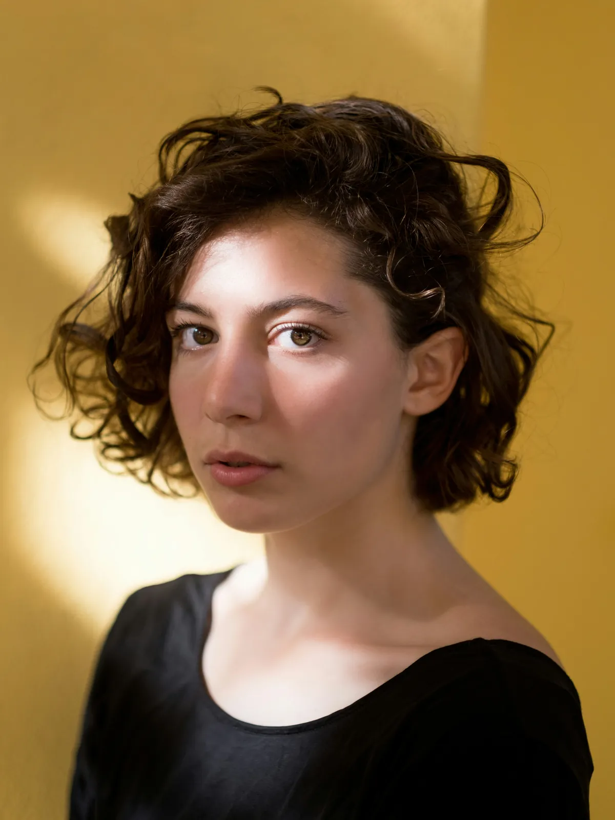 A portrait of a person with curly hair on a plain yellow background