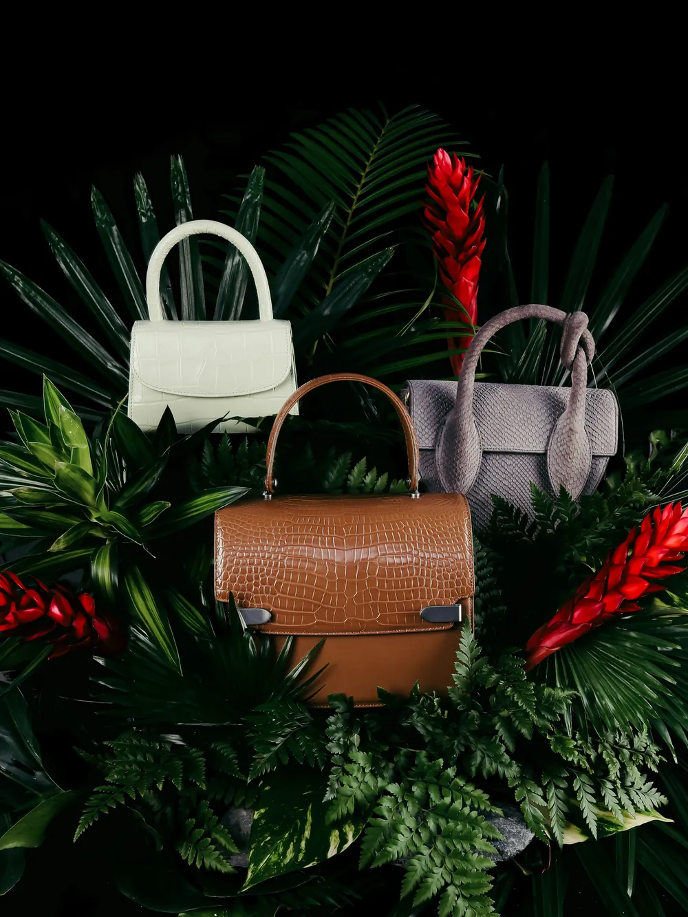 Three leather handbags among tropical leaves