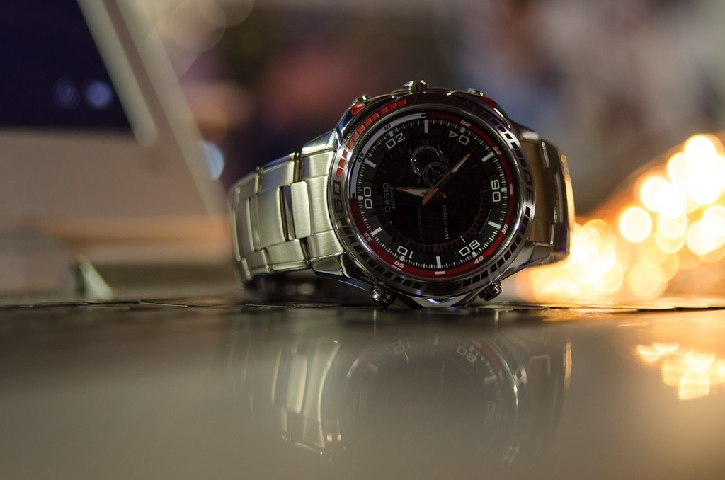 A steel wristwatch on a stand in front of a dark, blurred background